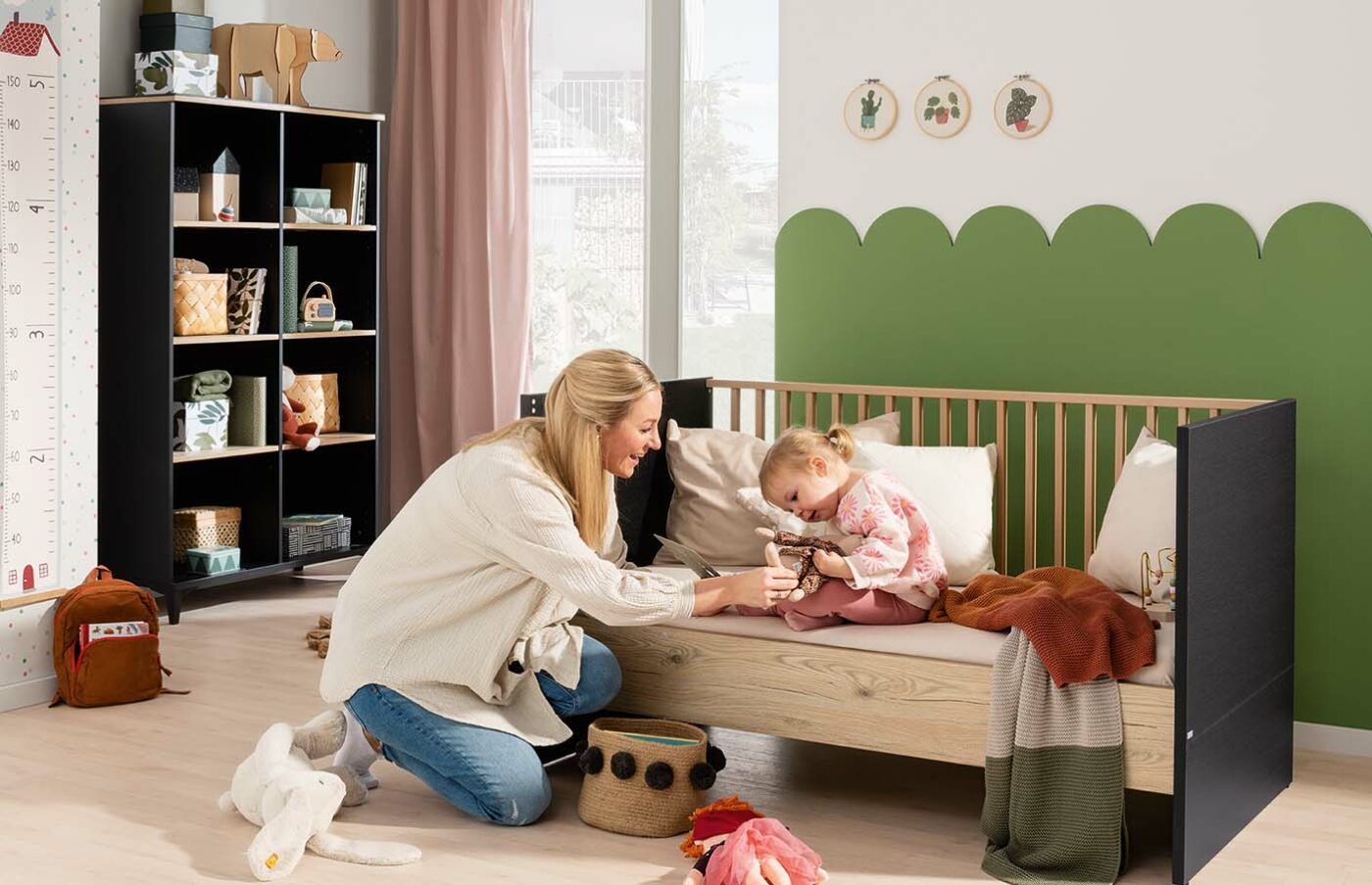 Mutter und Kind spielen im PAIDI Tomke Babyzimmer, hierin stehen ein Babybett und ein Regal